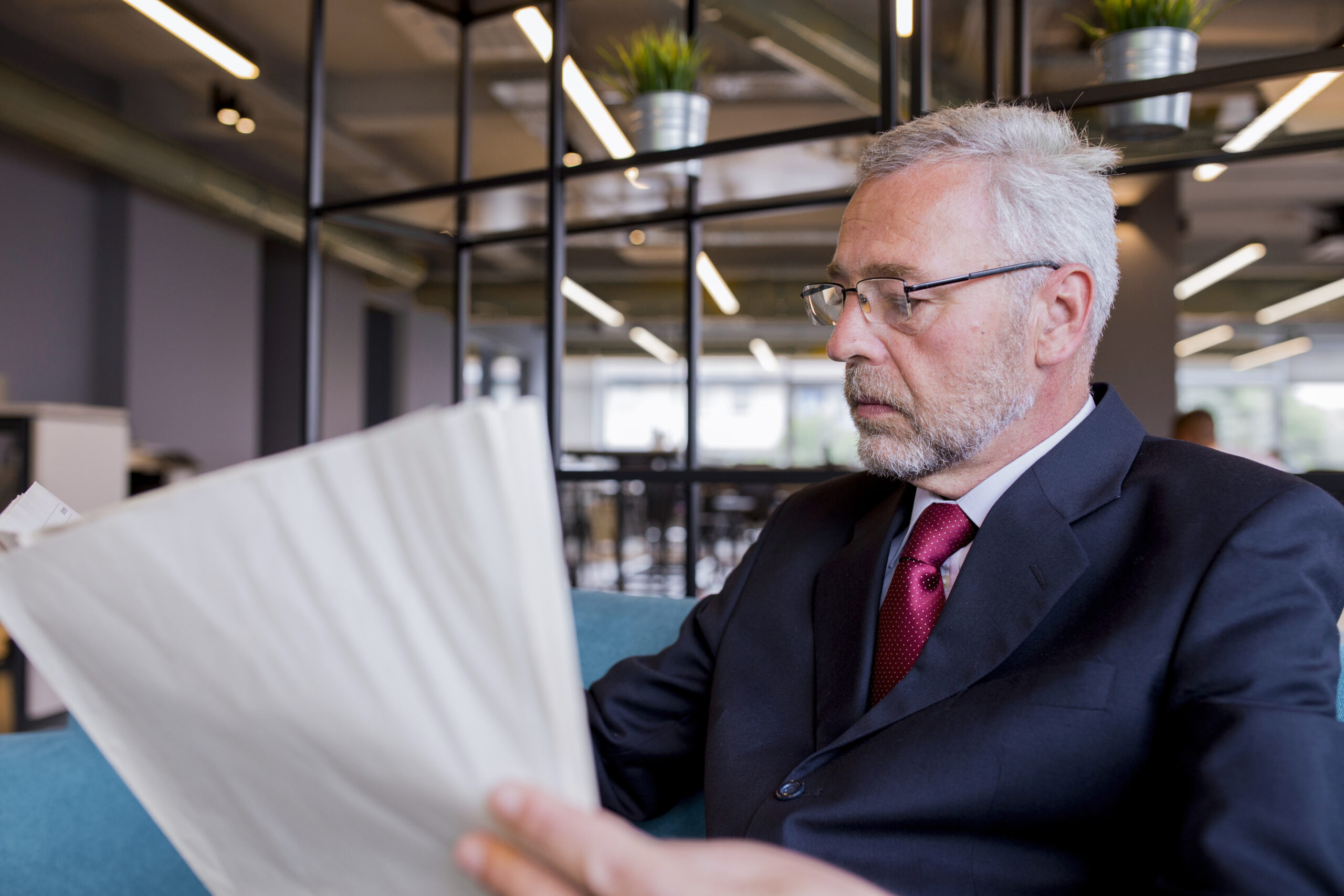 senior-businessman-sitting-reading-newspaper-office